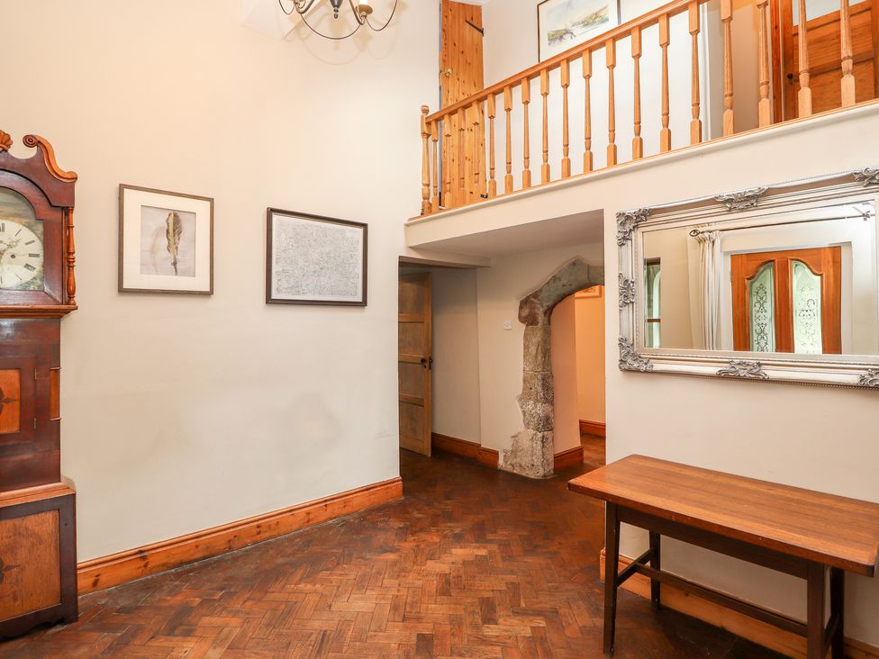 A hallway with a wooden grandfather clock two framed pictures a wooden table a large mirror and a wooden staircase railing at Abbey Cottage in Denbigh