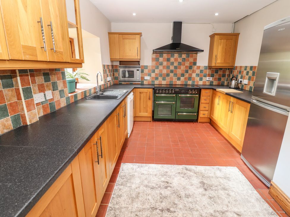 A kitchen with wooden cabinets a black countertop a green oven a stainless steel refrigerator and a tiled backsplash at Abbey Cottage in Denbigh