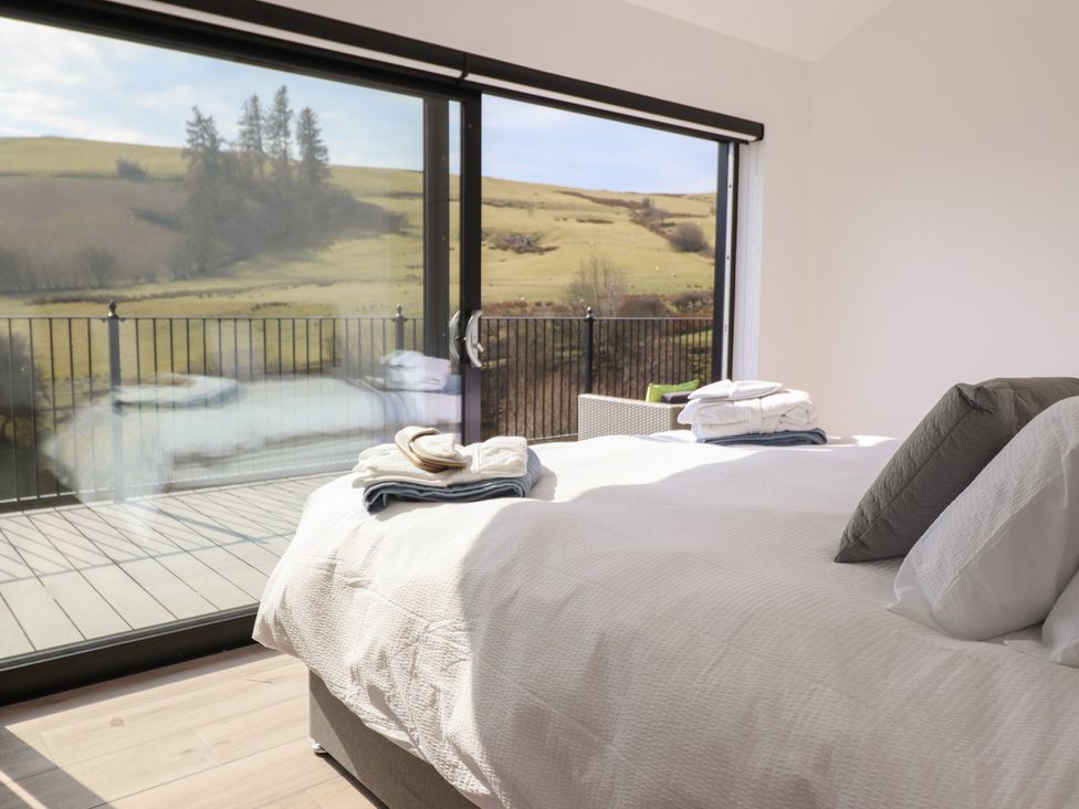 A bedroom with a bed near large glass sliding doors overlooking a balcony and countryside at The Sheep Shed in Llanrhaeadr-Ym-Mochnant