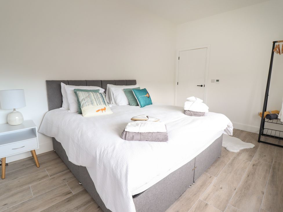 A bedroom with a large bed with pillows and folded towels a nightstand with a lamp and a clothes rack at The Sheep Shed in Llanrhaeadr-Ym-Mochnant