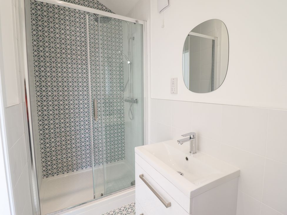 A bathroom with a shower enclosure featuring patterned tiles and a white sink with a mirror above at The Sheep Shed in Llanrhaeadr-Ym-Mochnant
