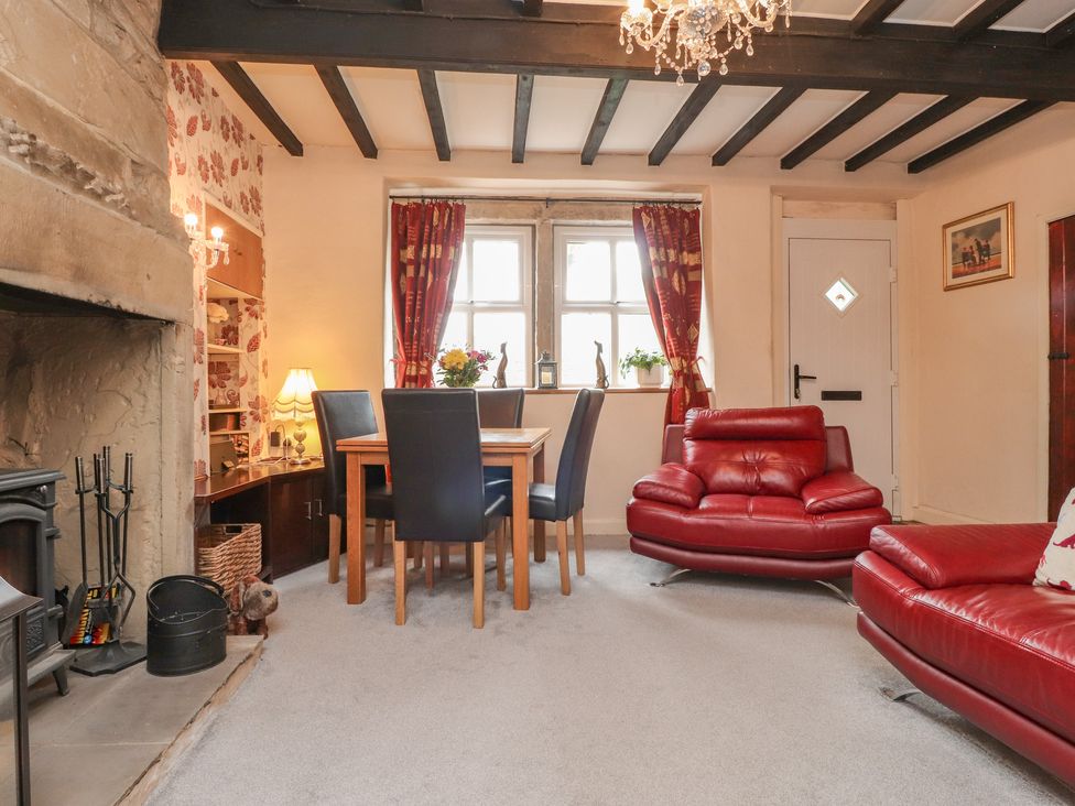 A living room with a stone fireplace a wooden dining table with black chairs red leather sofas and red curtains at Cobblers Cottage in Haworth