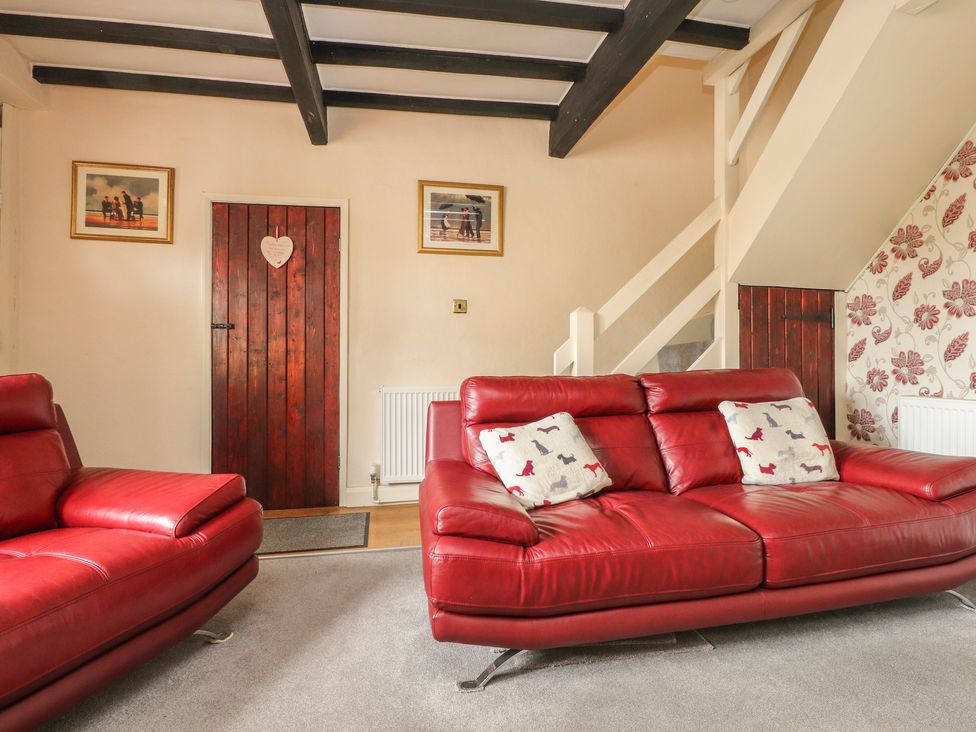 A living room with two red leather sofas and a wooden door at Cobblers Cottage in Haworth