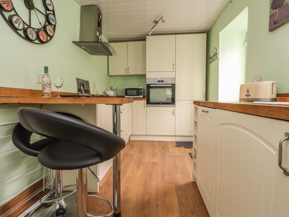 A kitchen with cream cabinets wooden countertops a built in oven a microwave two black bar stools a wall clock and a toaster at Cobblers Cottage in Haworth