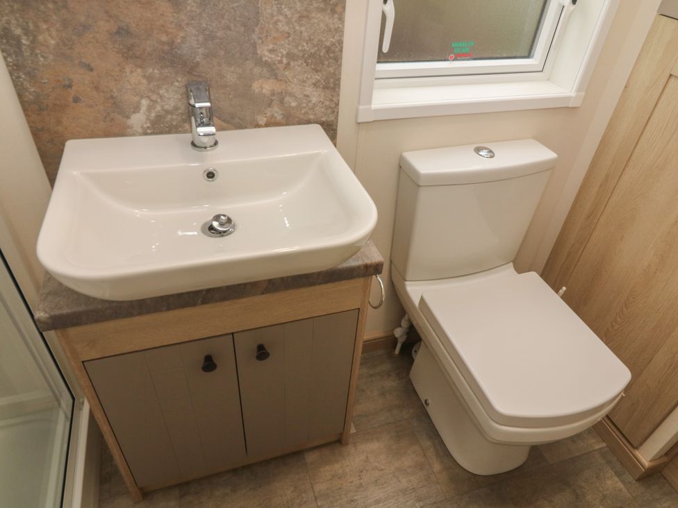 A bathroom with a sink on a cabinet next to a toilet under a window at Lancaster Lodge South Lakeland Leisure Village