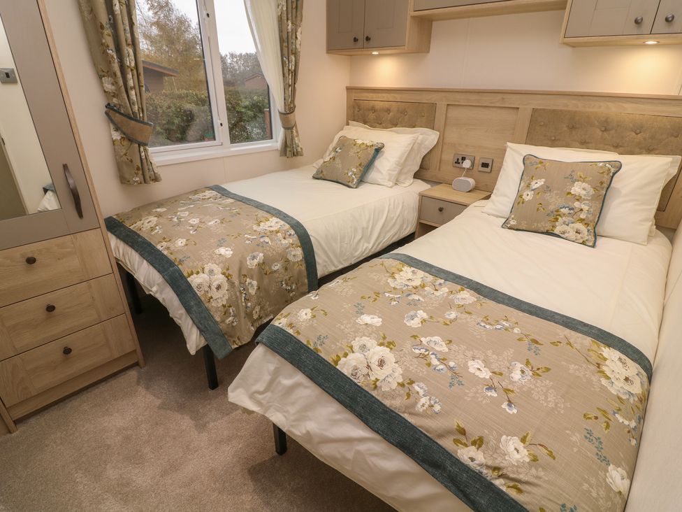A bedroom with two single beds with floral bed runners and cushions a window wardrobe and bedside table at Lancaster Lodge in South Lakeland Leisure Village