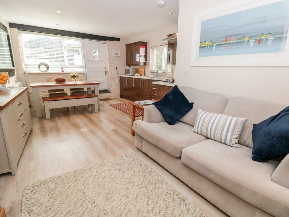 An open living and dining area with a beige sofa and cushions a dining table with chairs and a bench and a kitchen with wooden cabinets at Simples in Dartmouth