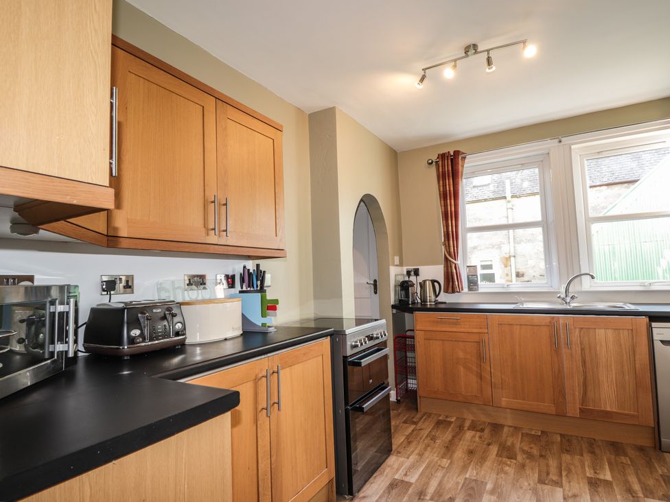 A kitchen with wooden cabinets black countertops a toaster bread box microwave stove and sink at 62 Society Street in Nairn