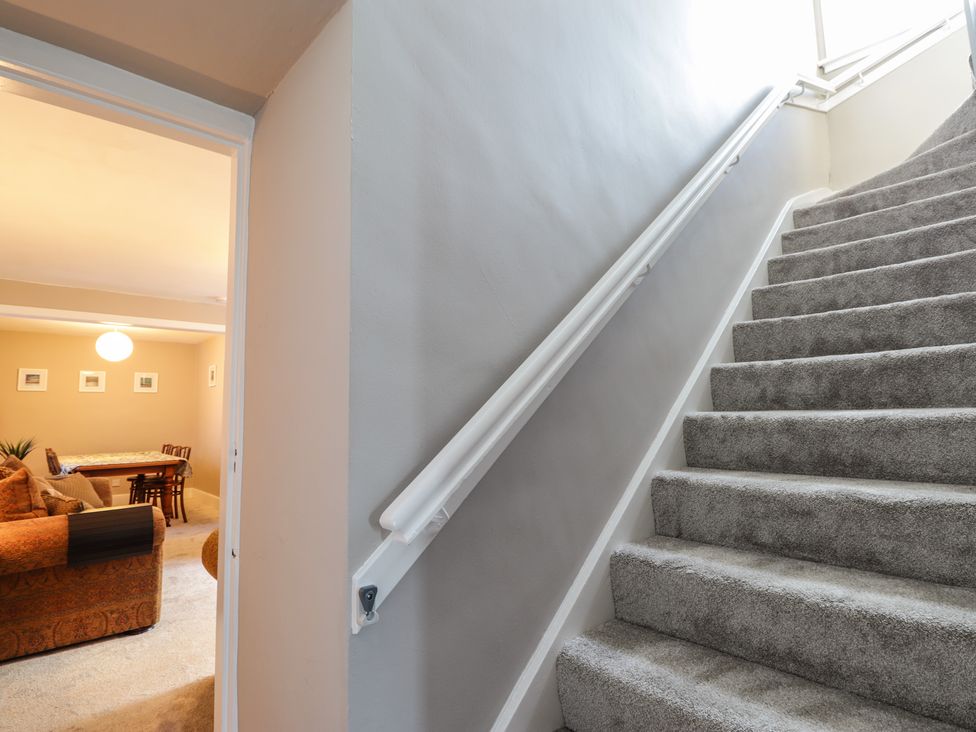 A carpeted staircase with a white handrail next to a room with an orange sofa and a dining table at 62 Society Street in Nairn