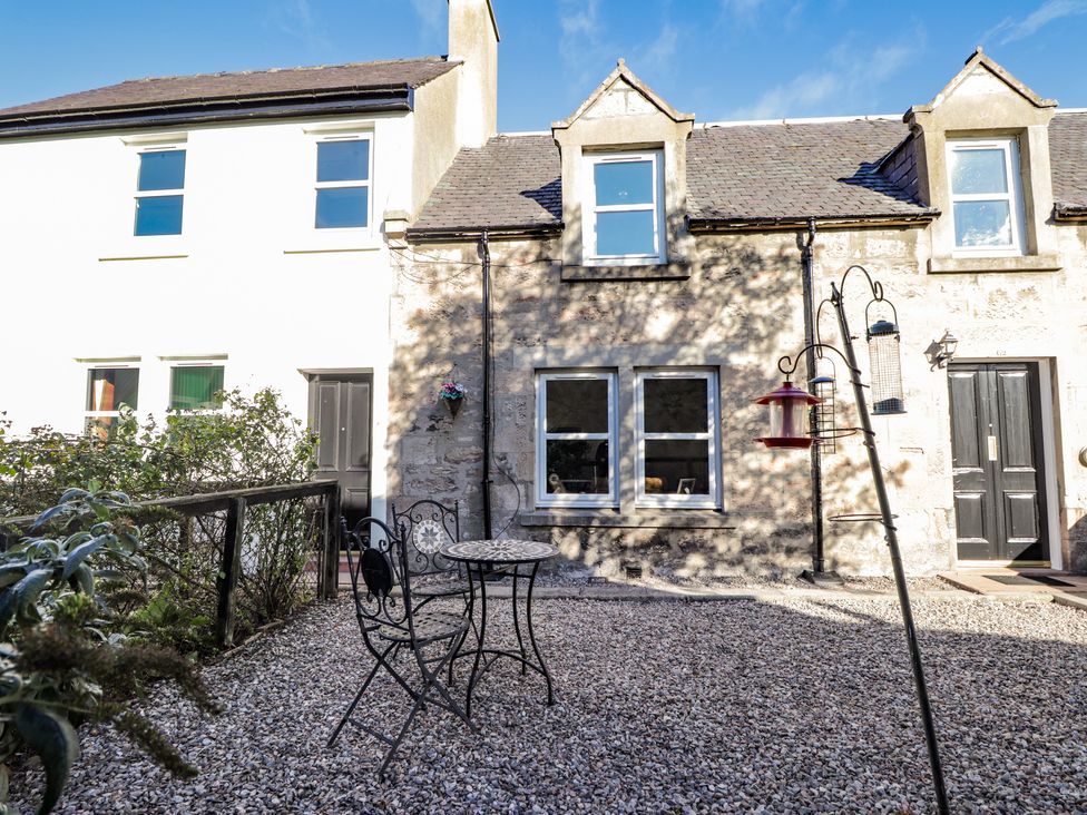 A gravel courtyard with metal table and chairs and bird feeders outside stone cottages at 62 Society Street in Nairn