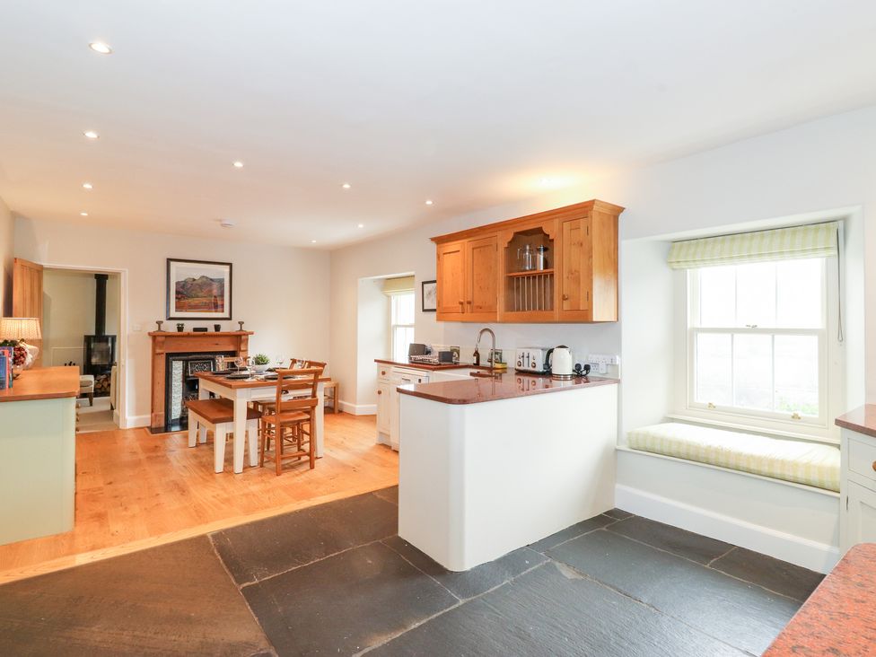 A kitchen and dining area with wooden cabinets dining table and window seat at Rose Cottage At Troutbeck in Troutbeck