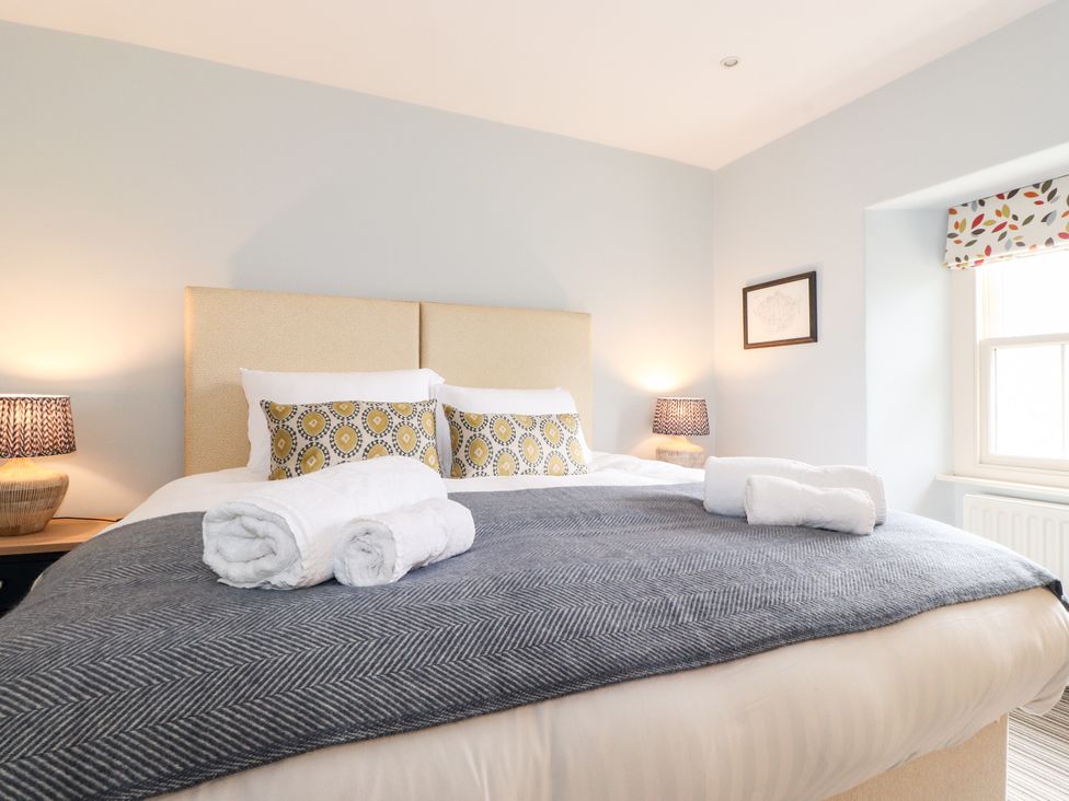 A bedroom with a bed with patterned pillows and rolled towels on a blanket at Rose Cottage At Troutbeck in Troutbeck
