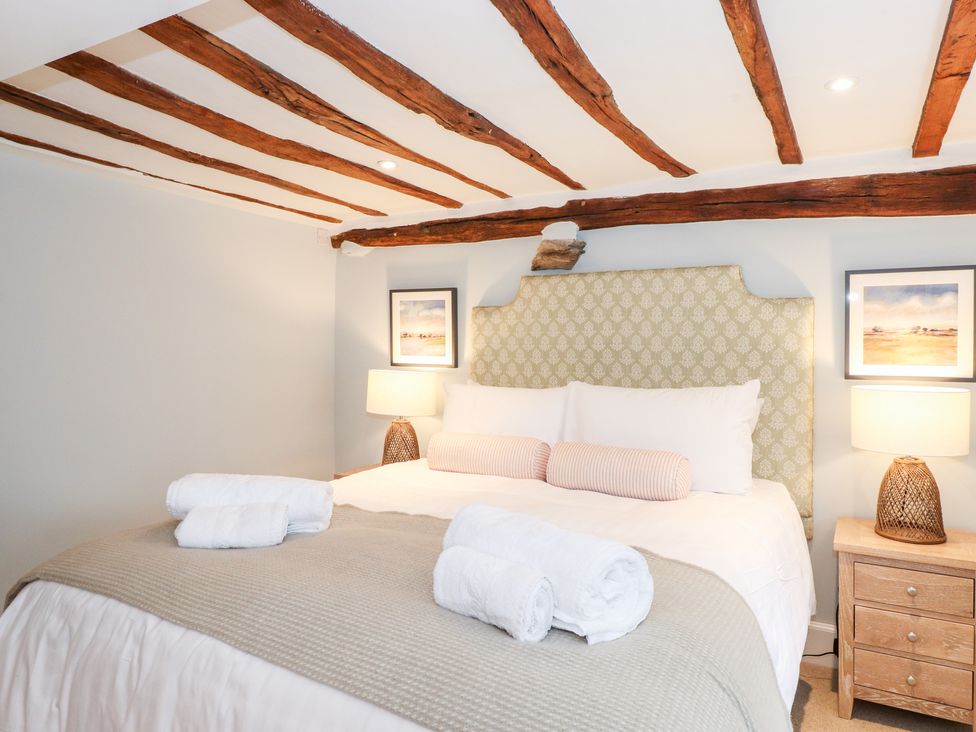 A bedroom with a bed with rolled towels on it two bedside tables with lamps and wooden ceiling beams at Rose Cottage At Troutbeck in Troutbeck