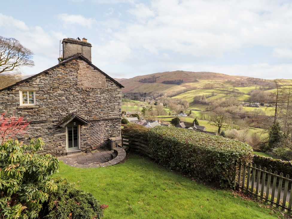 Stone house with small patio door next to a lawn and hedge overlooking hills and countryside at Rose Cottage At Troutbeck in Troutbeck