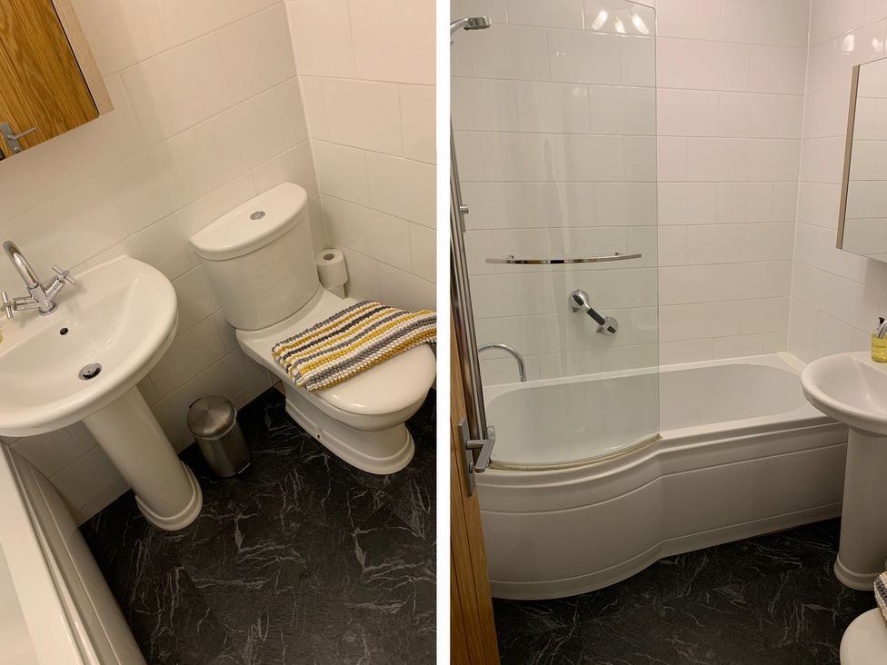 A bathroom with a toilet a sink a bathtub with a shower screen and a wooden door at Seashells Cottage in Lytham St Annes