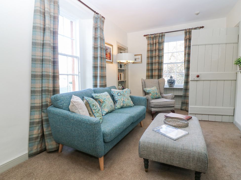 A sitting room with a blue sofa with floral cushions an armchair an ottoman a lamp and plaid curtains at Pear Cottage - Priorwood Garden in Melrose