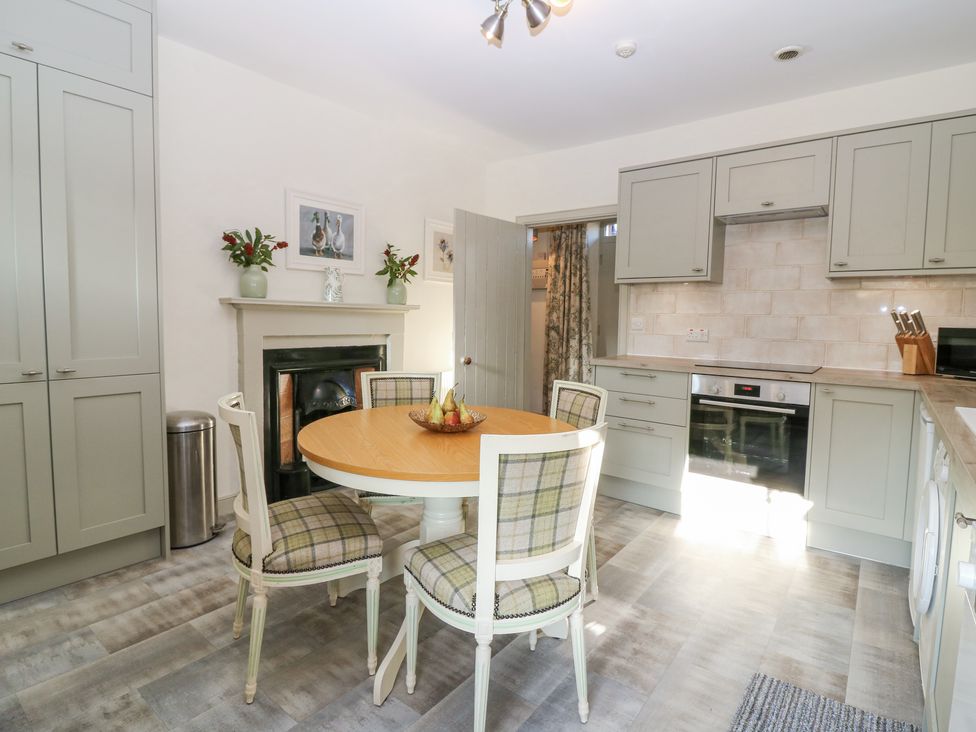 A kitchen with a round wooden table and four chairs a fireplace and built in cabinets at Pear Cottage - Priorwood Garden in Melrose