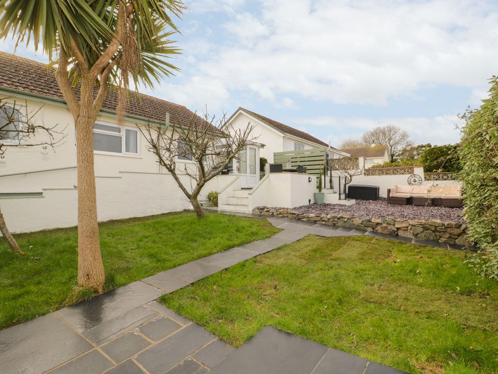 A backyard with grass trees and a stone pathway leading to a patio with outdoor seating at Hardy Cottage in Benllech