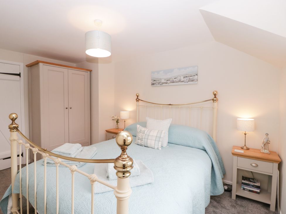 A bedroom with a bed covered in blue bedding two bedside tables with lamps and a wardrobe at Blueberry Cottage in Cerne Abbas