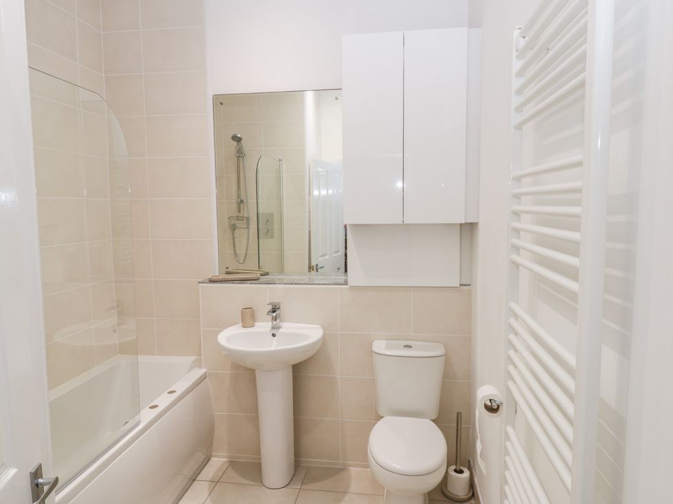 A bathroom with a bathtub and shower, a pedestal sink, a toilet, a wall-mounted cabinet, and a towel radiator at Bluewater View in Saltburn-By-The-Sea