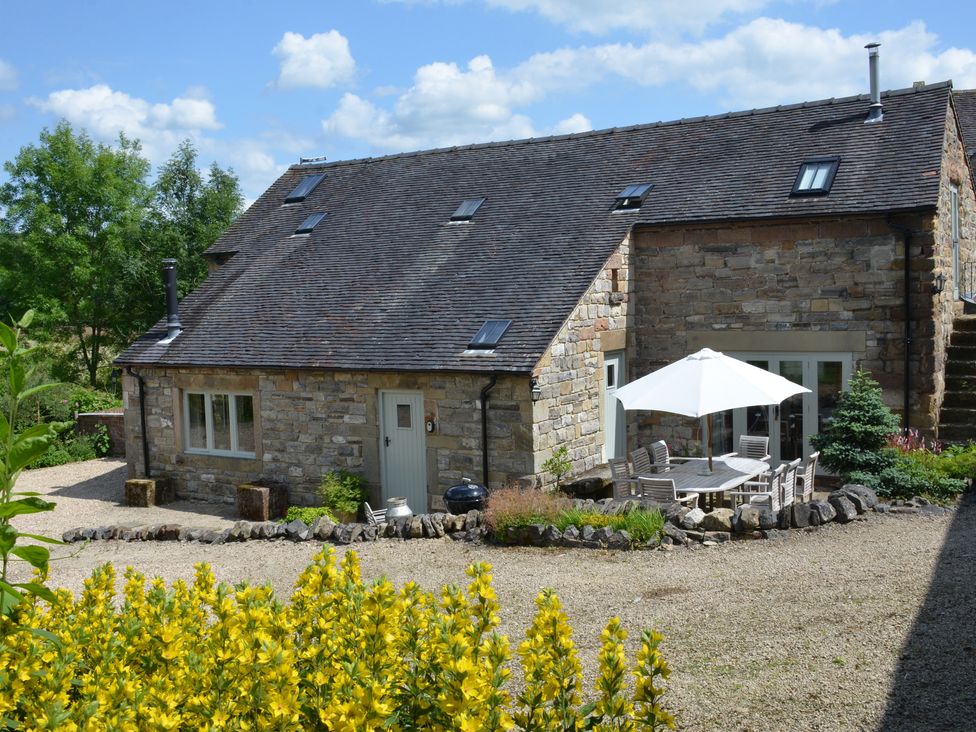 A stone house with multiple skylights a gravel yard and outdoor dining table with umbrella at Green Farm Stables in Hognaston near Carsington Water