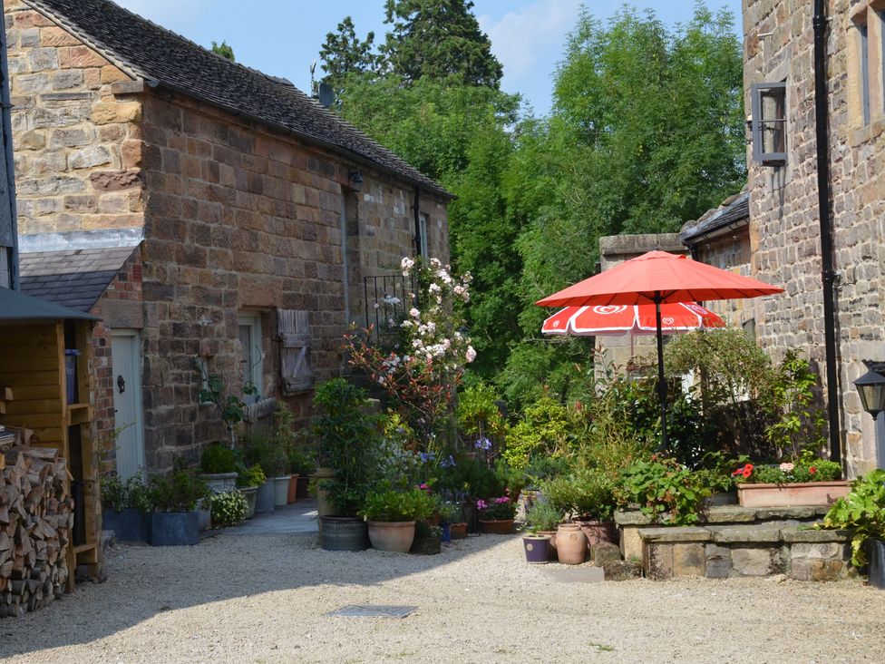 An outdoor courtyard with stone buildings plants in pots and a red umbrella at Green Farm Stables Hognaston near Carsington Water