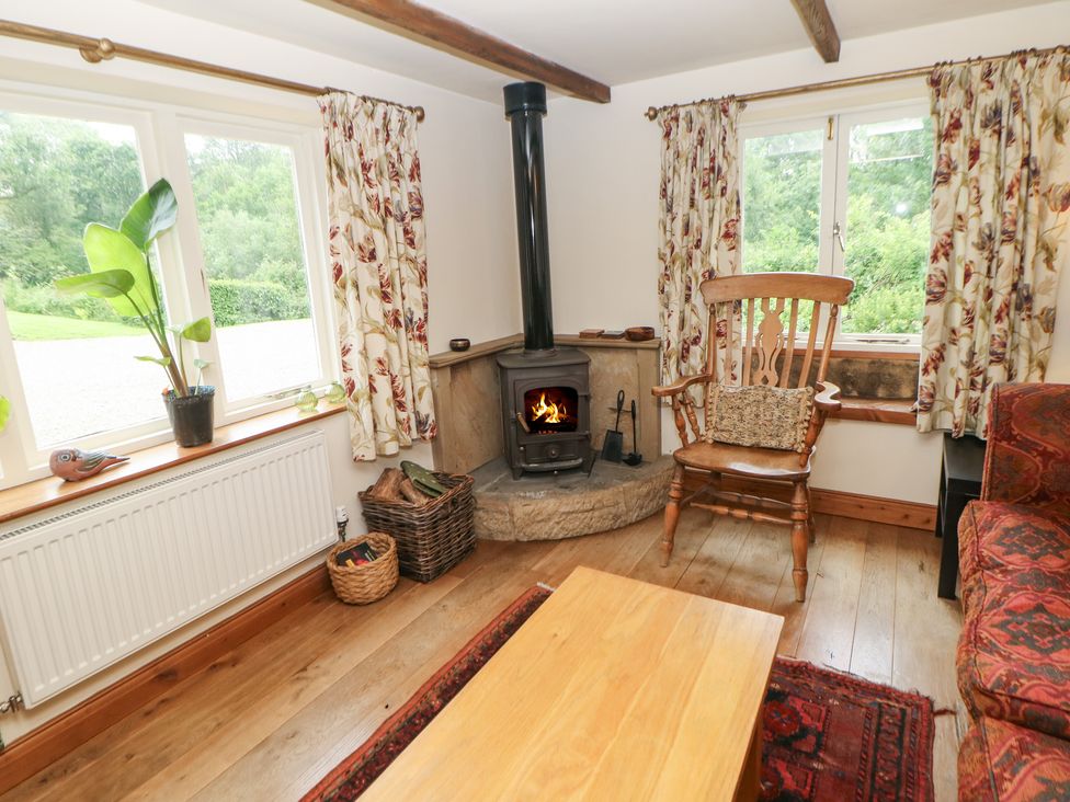 A living room with a wood burning stove wooden chair and table and floral curtains at Green Farm Stables Hognaston near Carsington Water