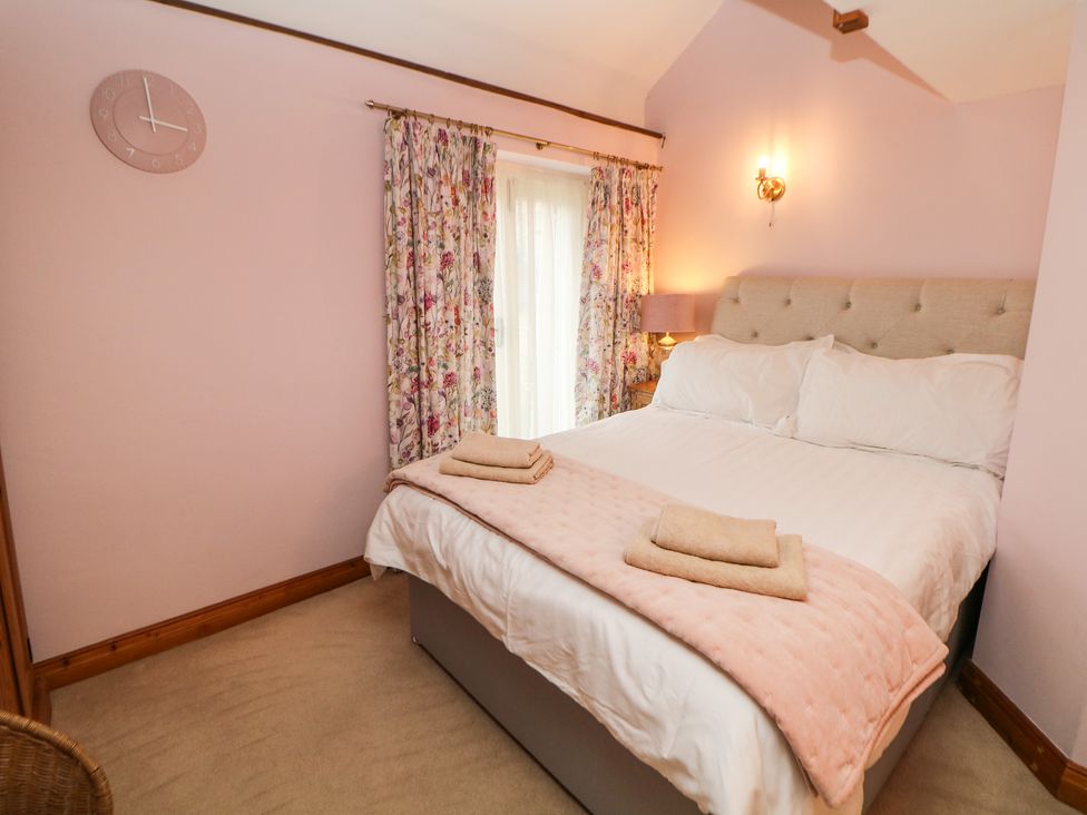 A bedroom with a double bed white bedding pink blanket folded towels floral curtains and a wall clock at Green Farm Stables in Hognaston near Carsington Water
