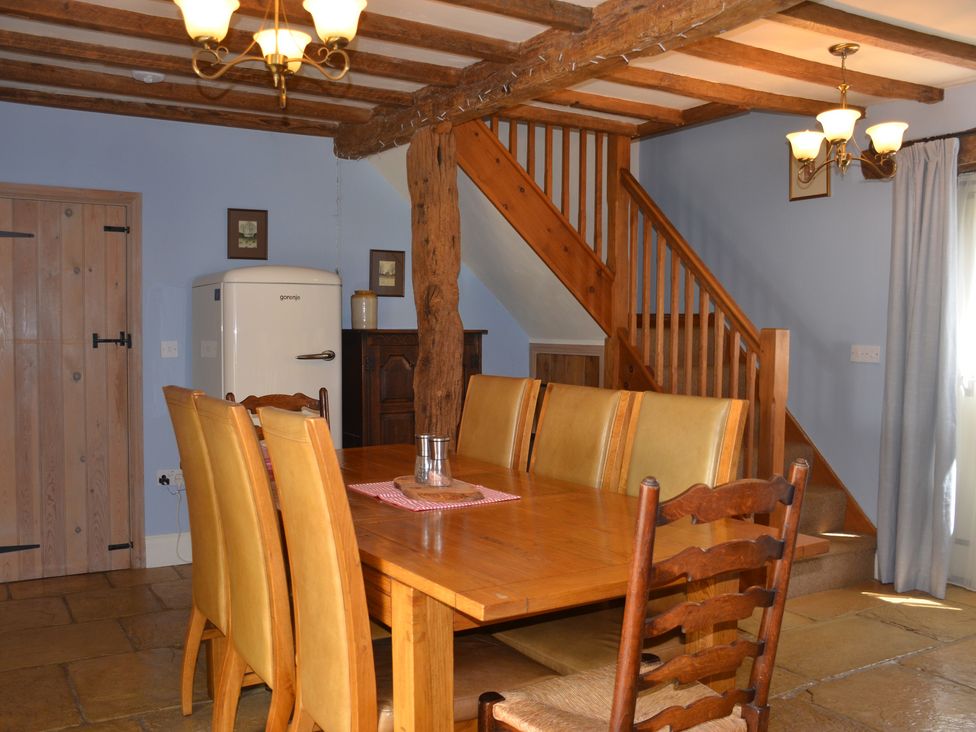 A dining room with wooden table and chairs near wooden stairs and a white refrigerator at Green Farm Stables in Hognaston near Carsington Water