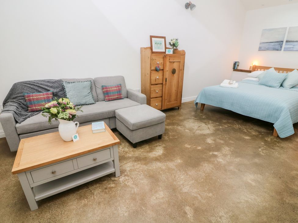 A bedroom with a gray sofa, coffee table, wooden wardrobe, and a bed with blue bedding at Horncop Nook in Kendal