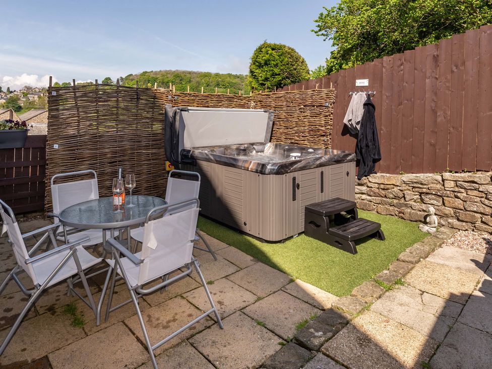 An outdoor patio with a hot tub, glass table with four chairs, and a bottle of wine at Ramblers Retreat in Settle