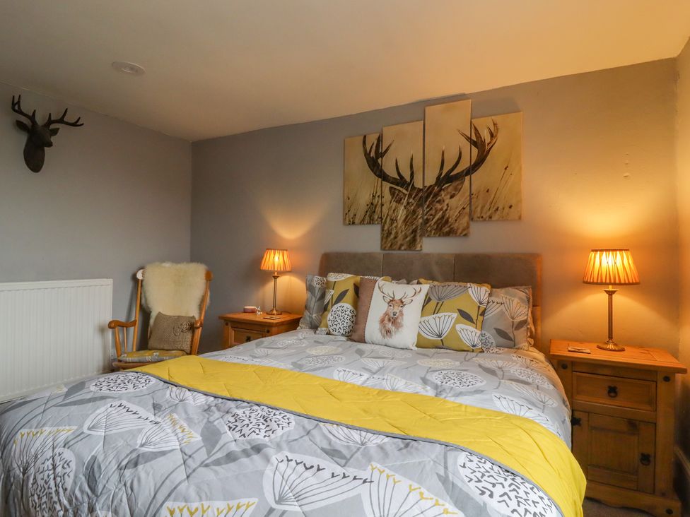 A bedroom with a bed featuring patterned bedding and deer-themed pillows two bedside tables with lamps and a wooden chair with a cushion at Ramblers Retreat in Settle