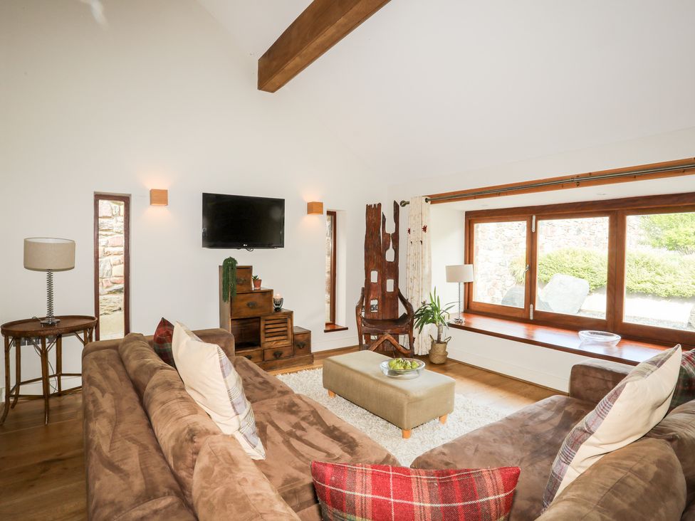 A living room with brown sofas and a wall mounted TV at Clynnog House in Dwyran near Newborough