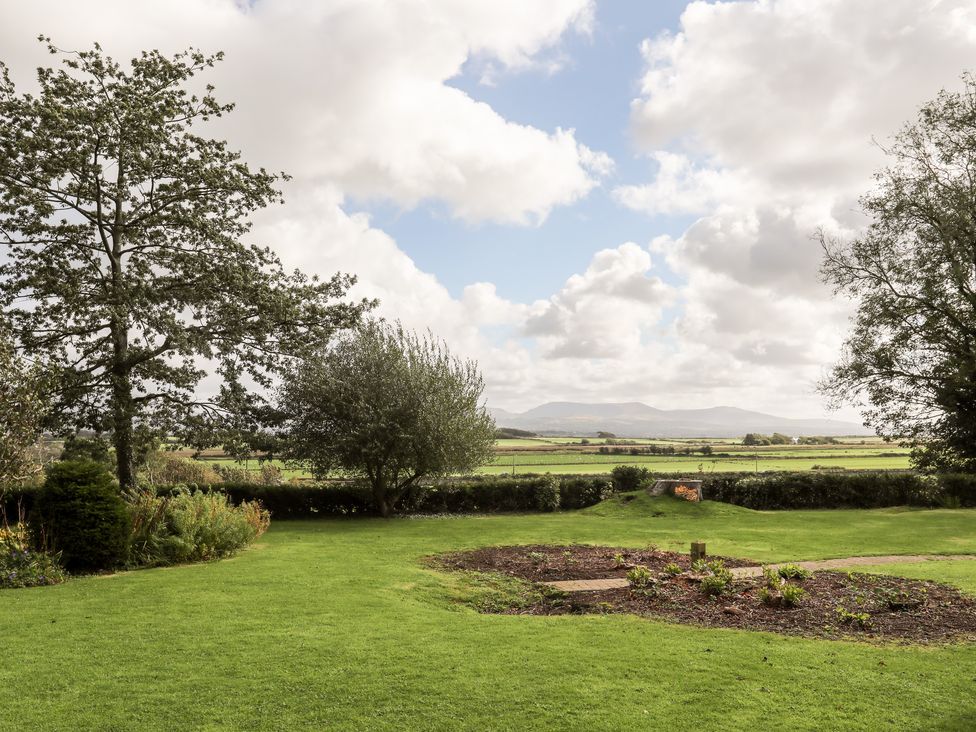 A garden with grass trees and flowerbeds overlooking fields and mountains at Clynnog House in Dwyran near Newborough