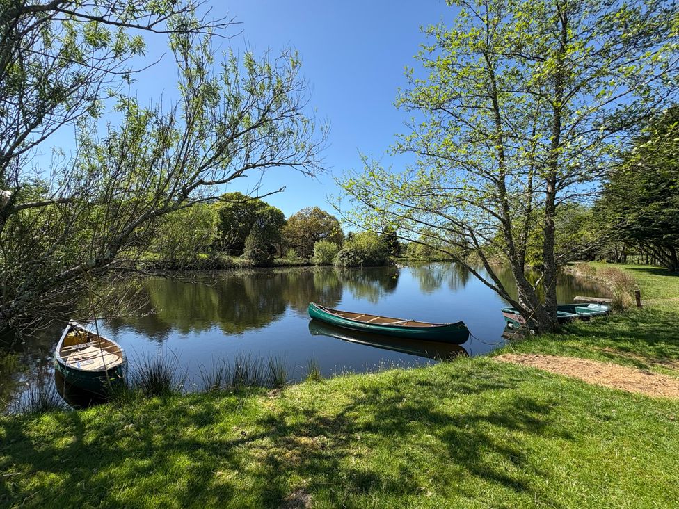 A river with small boats on the bank and trees around at Garden Cottage in Garndolbenmaen near Tremadog