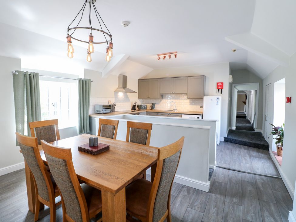 A dining area with wooden table and chairs next to a kitchen with gray cabinets and appliances at The Loft at The George in Clay Cross