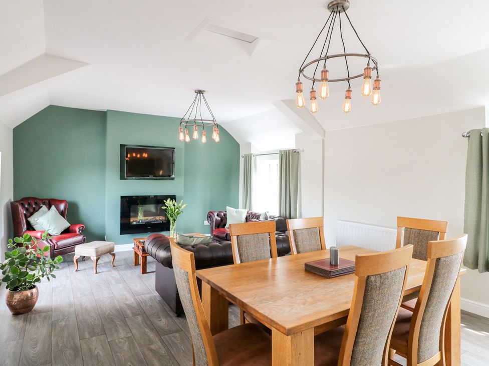 A dining table with chairs and a seating area with armchairs television and green accent wall at The Loft at The George in Clay Cross