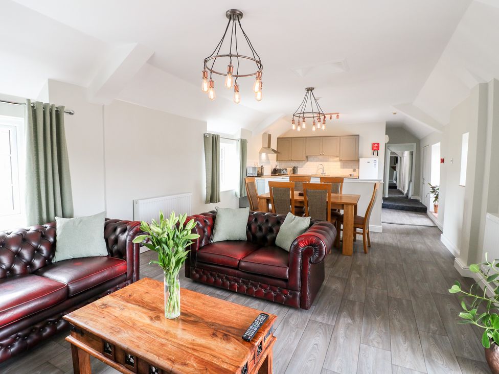 A living room with two leather sofas a wooden coffee table and kitchen with dining table at The Loft at The George in Clay Cross