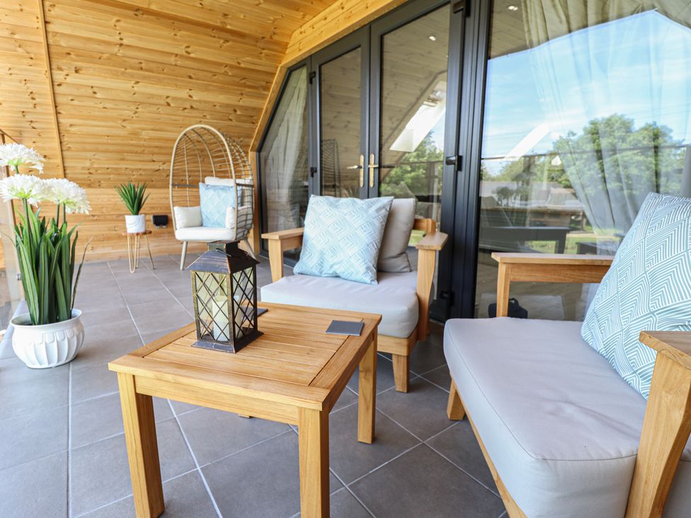 A covered patio with wooden chairs and table with cushions and a hanging chair at Lake View Lodge in Thorpe-On-The-Hill