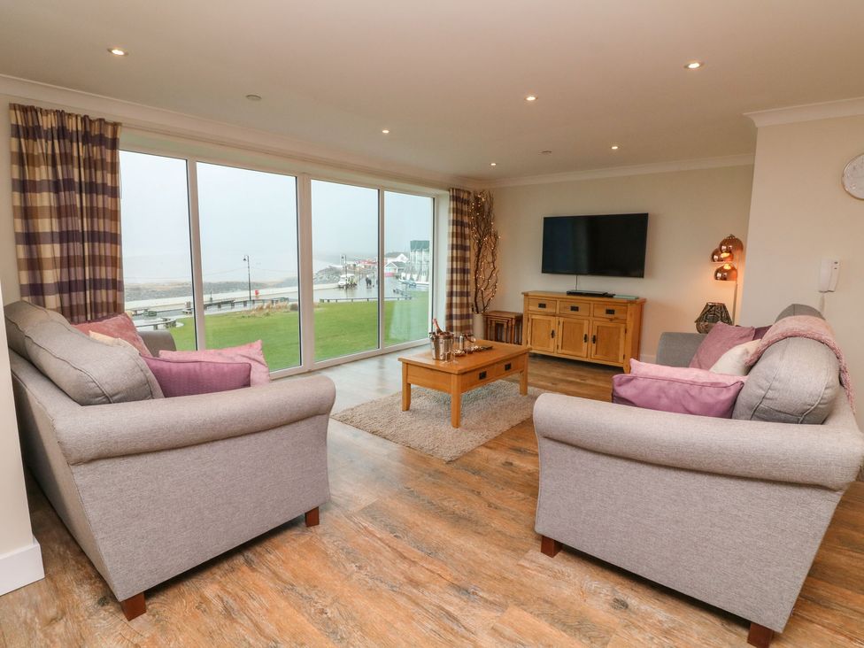 A living room with two grey sofas and a wooden coffee table facing a wall-mounted TV by the window at The Lobster Pot in Westward Ho