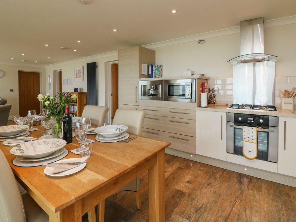 A kitchen and dining area with a wooden table set with plates glasses and wine and a built in oven microwave and coffee machine at The Lobster Pot in Westward Ho