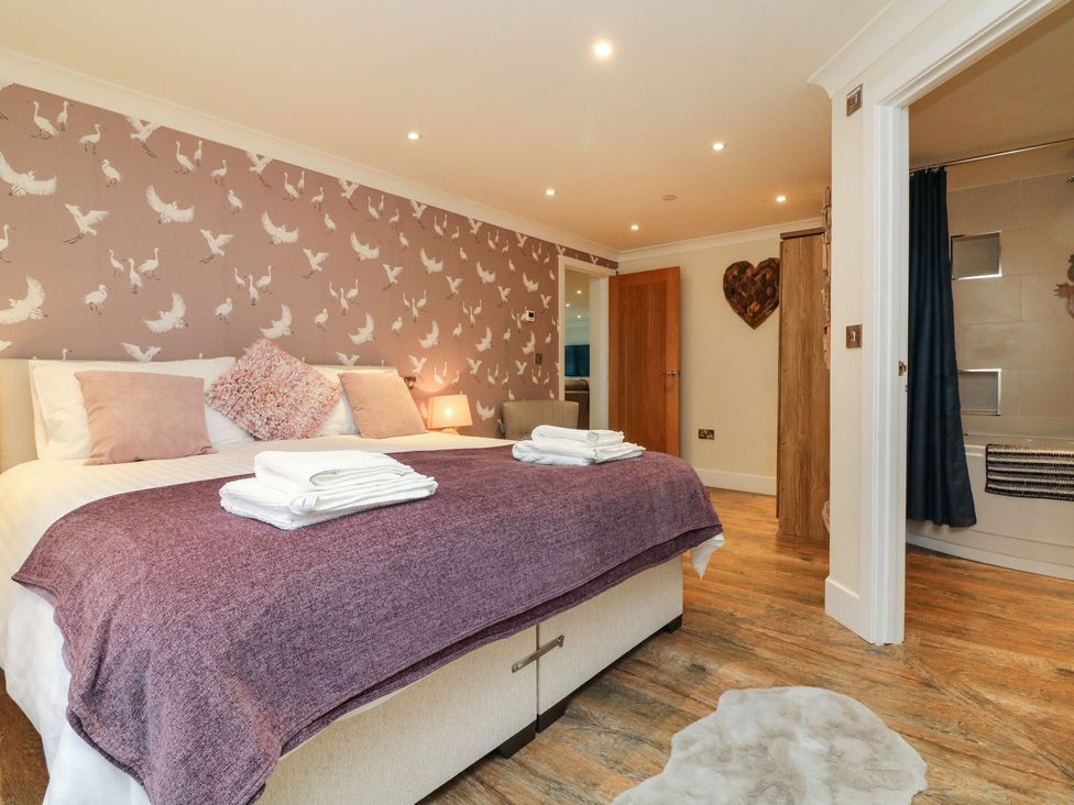 A bedroom with a double bed towels bedside lamp wooden floor and an adjacent bathroom at The Lobster Pot in Westward Ho