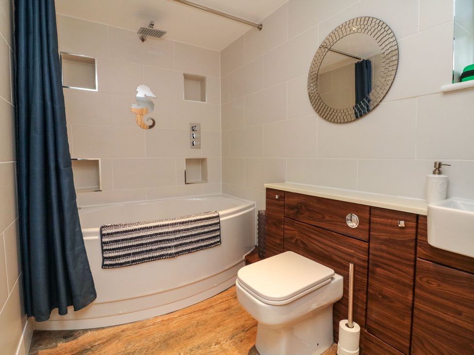 A bathroom with bathtub shower curtain toilet wooden cabinets and round mirror at The Lobster Pot in Westward Ho