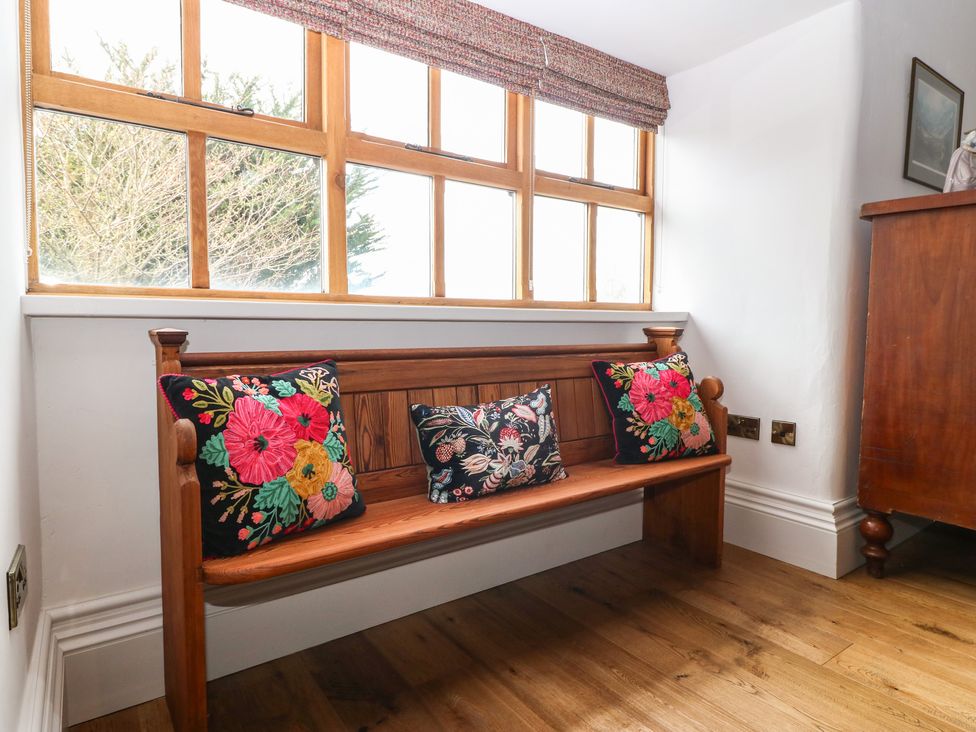 A wooden bench with three floral cushions under a window in a room at Balog Farm in Amlwch
