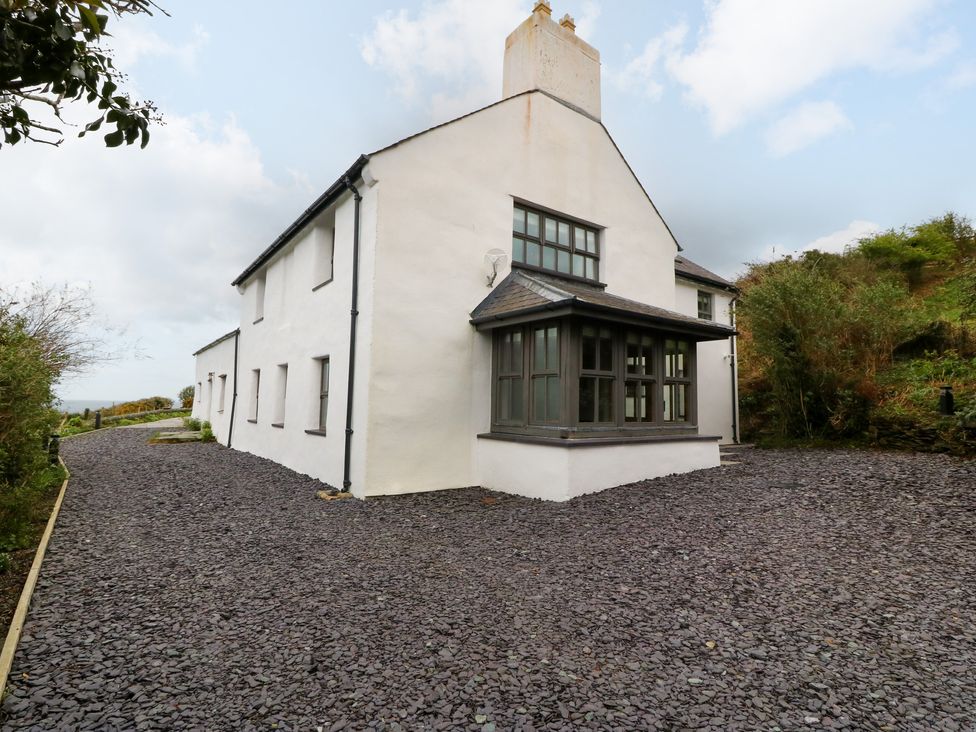 The exterior of a two story white house with multiple windows and a gravel driveway at Balog Farm in Amlwch