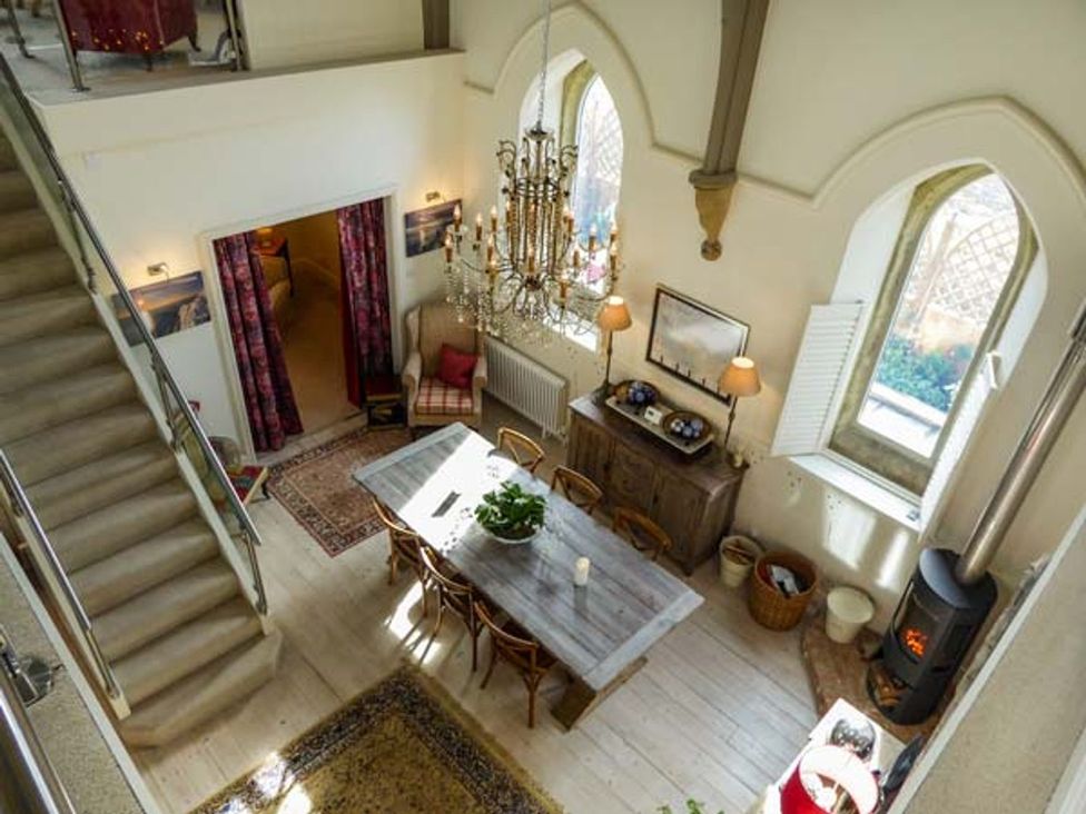 A dining area with a wooden table and chairs a chandelier and a stove by the window at Chapel House in Chale