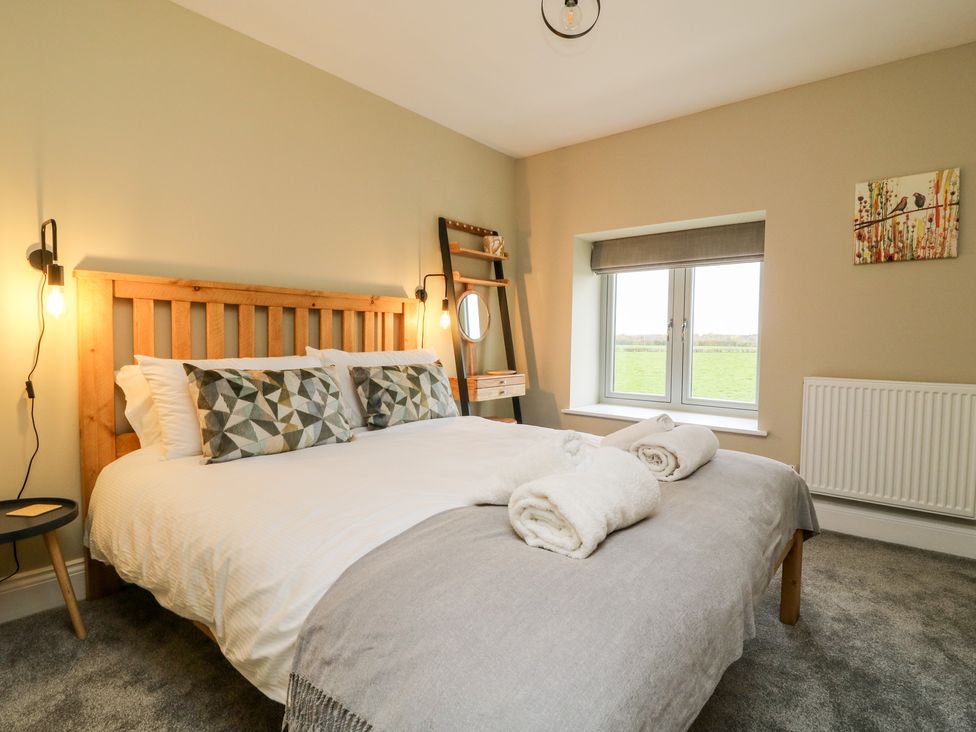 A bedroom with a wooden bed frame and geometric pillows a window a small side table and rolled towels on the bed at The Cart House in Wilberfoss