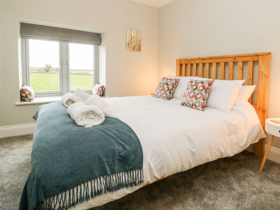 A bedroom with a wooden bed frame white bedding patterned pillows and towels on a blue throw at The Cart House in Wilberfoss