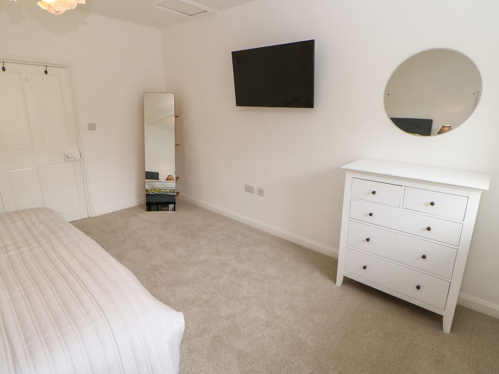 A bedroom with a white dresser and round mirror a wall-mounted tv and a full-length mirror at The Old Store 2 Alpine Terrace Reeth