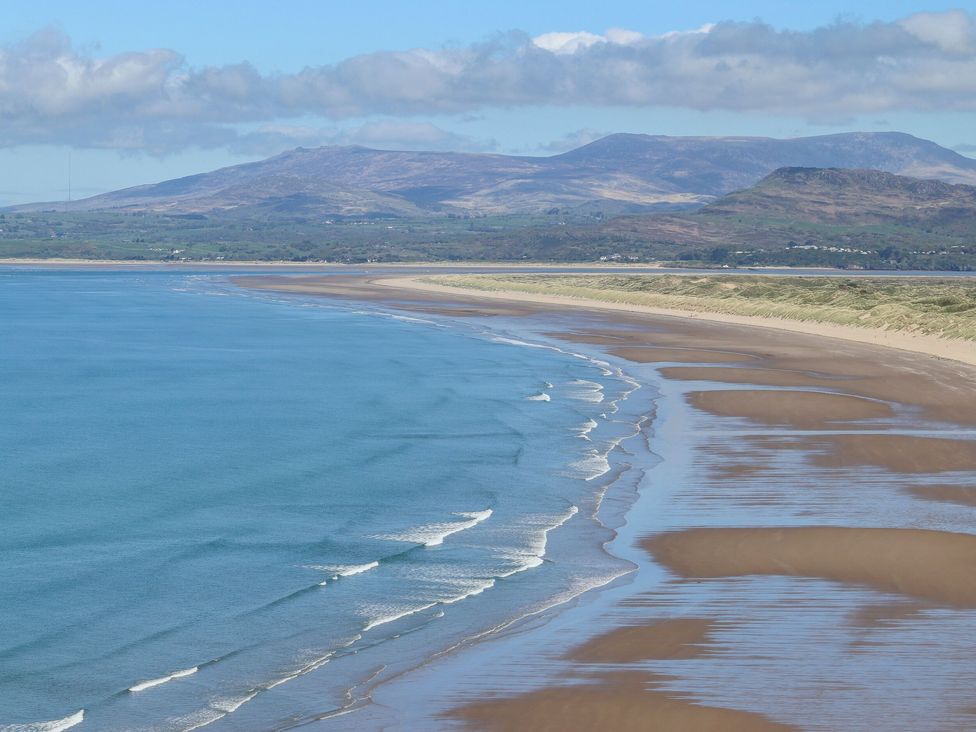 A beach with waves and sand dunes with mountains in the background at Plas Amherst in Harlech